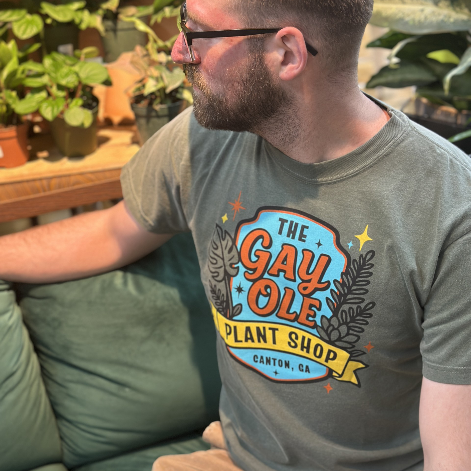 Man wearing a t-shirt with 'The Gay Ole Plant Shop' design in a plant store.